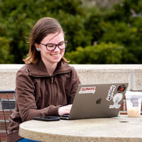 Student works on her laptop at a table outside.