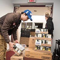 Students lift boxes of cans at a food pantry.