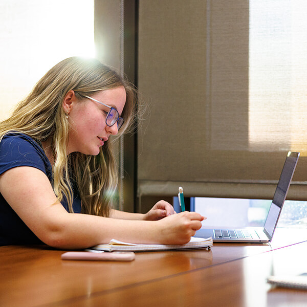 A student writes on a notebook and looks at laptop while studying in the library.