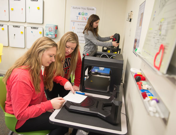 Three student teachers work with 3D printers.