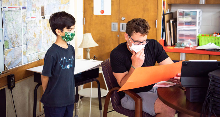 An elementary student shows his student teacher the work he has done.