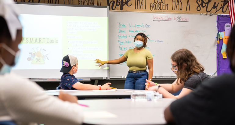 Elementary student teacher stands at the projector teaching her students.