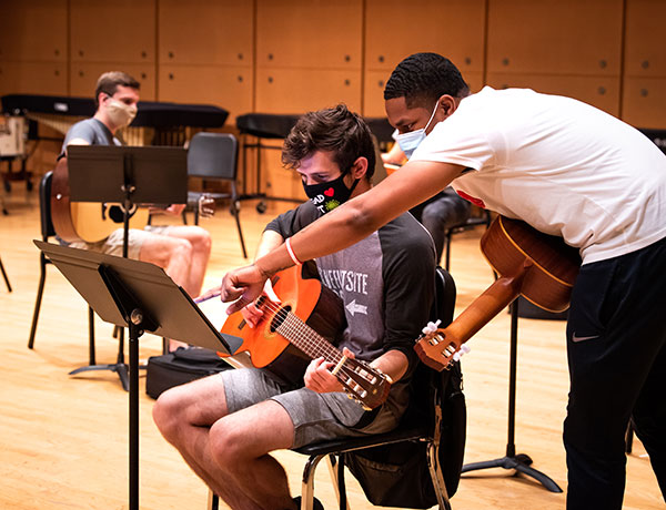 A guitar student helps his classmate read sheet music.