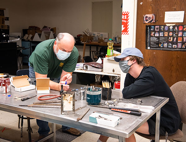 A professor teaches wood and metal design techniques to a student.
