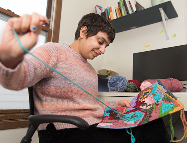 Female student stitches with yarn in an embroidery piece.
