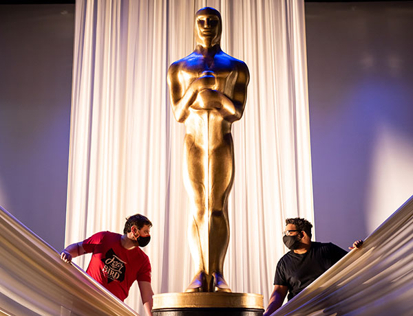 Two male students work in the scene shop on a golden statue.