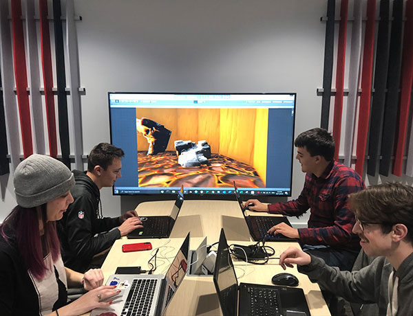 A group of four game design students sit at a table discussing their progress.