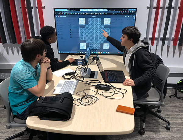 Three game design students discuss as one points to their design progress on a screen.