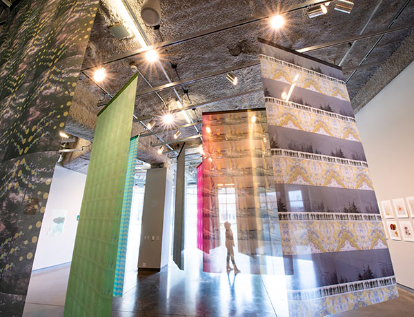 Colorful, patterned tapestries hang from a gallery ceiling.