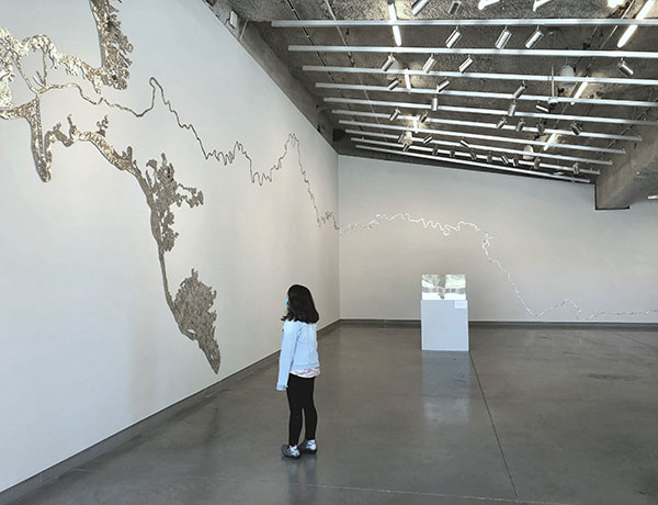 A gallery visitor observes Jen Bervin’s silk artwork “Shift Rotate Reflect” that travels across the gallery wall.