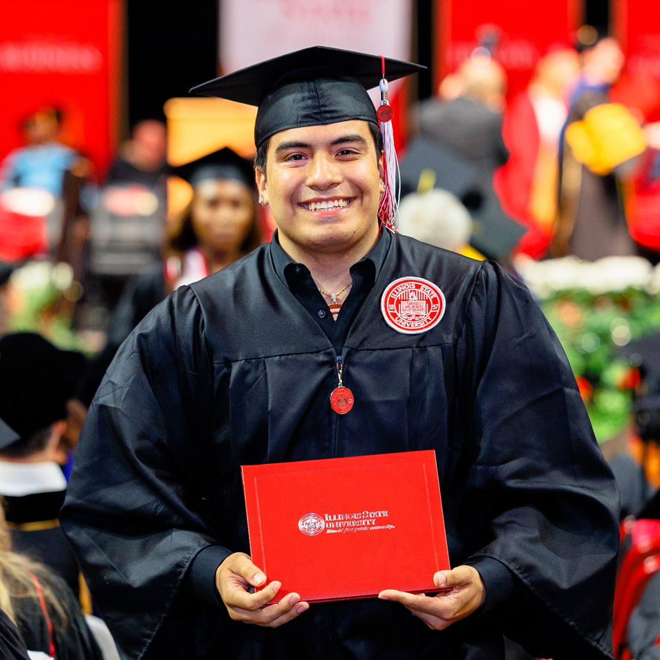 Student smiling holding a diploma cover at a commencement ceremony.