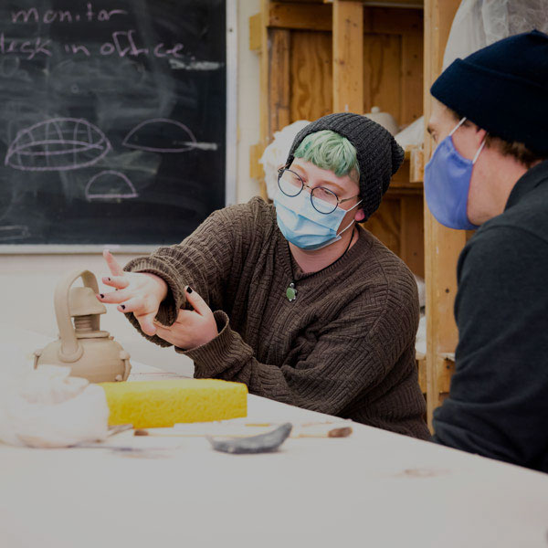 A ceramics student discusses their work with their professor.