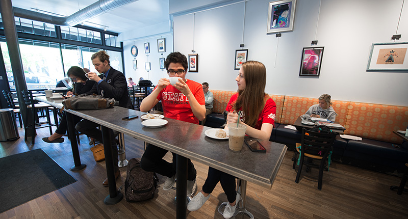Students drinking coffee at a raised table in the Coffee Hound.
