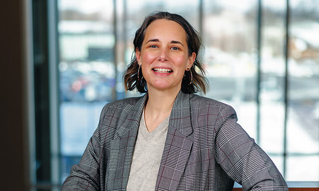 Person smiling indoors, wearing a gray plaid blazer.