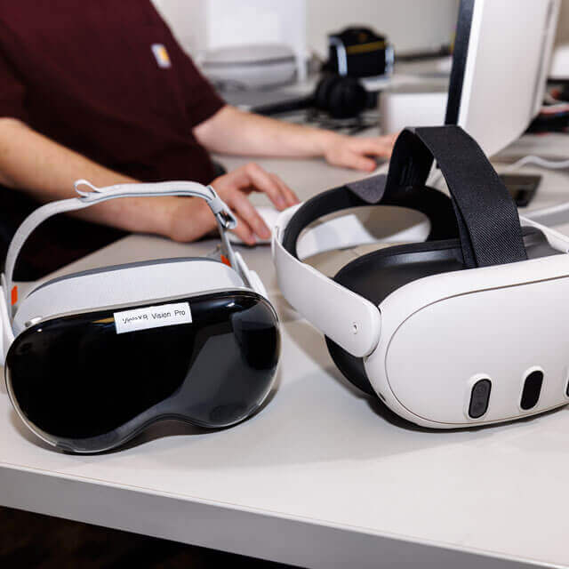 Two VR headsets on a desk, one labeled 'Vision Pro.'
