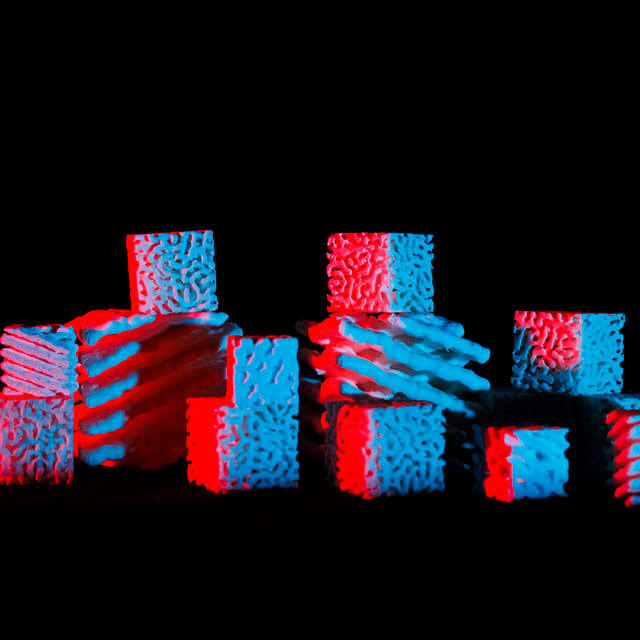3D-printed cubes with porous structures, illuminated by red and blue lights against a black background.