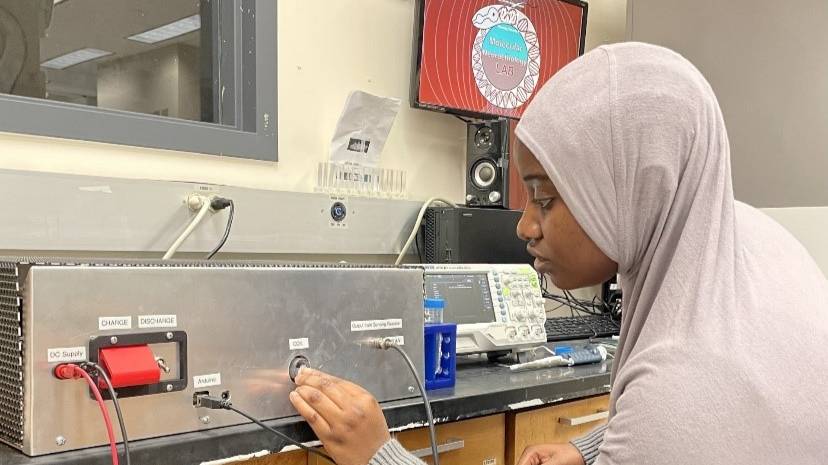 female lab student wearing a head covering adjusts lab equipment.