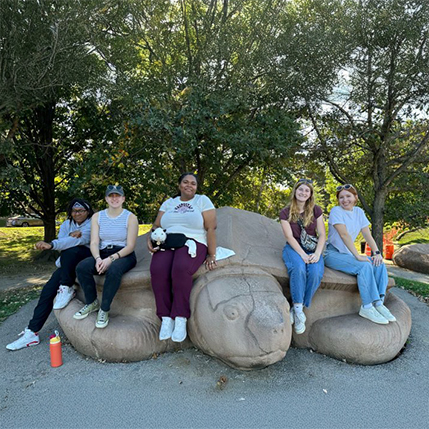 a group of students sitting on a large, decorative, concrete turtle at the St. Louis zoo