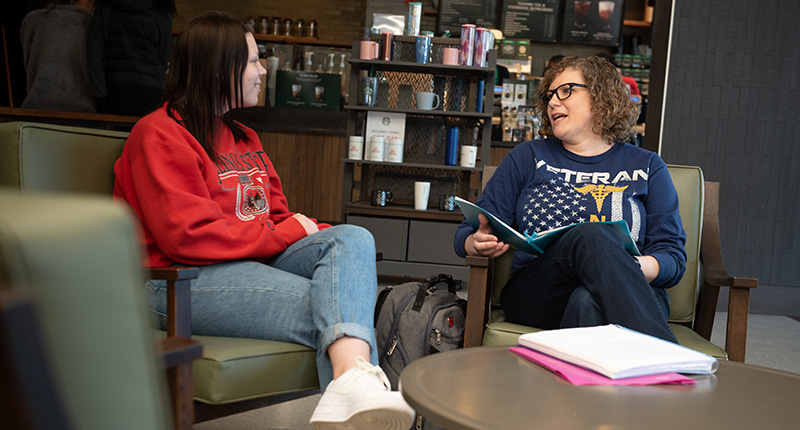 Two females in comfortable chairs, chatting in a coffee shop.